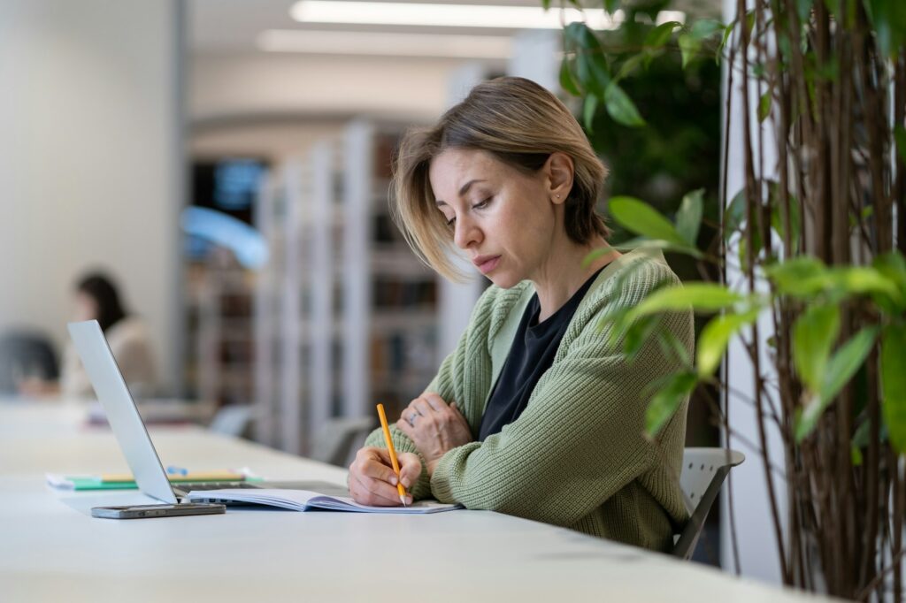 Academic career. Female university professor taking notes in day planner while sitting in library