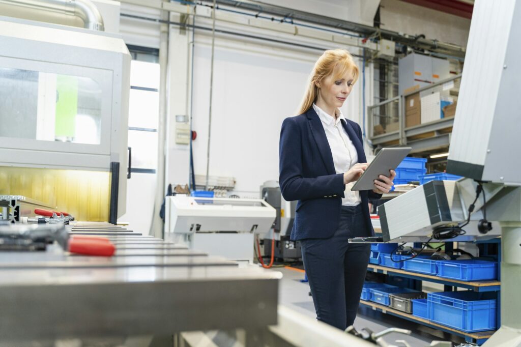 Businesswoman using tablet at machine in factory