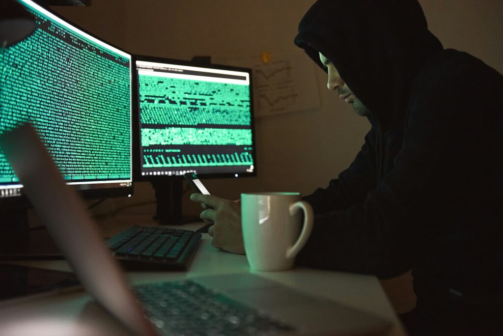 Computer security. Young man in black hoodie using multiple computers and his smartphone for