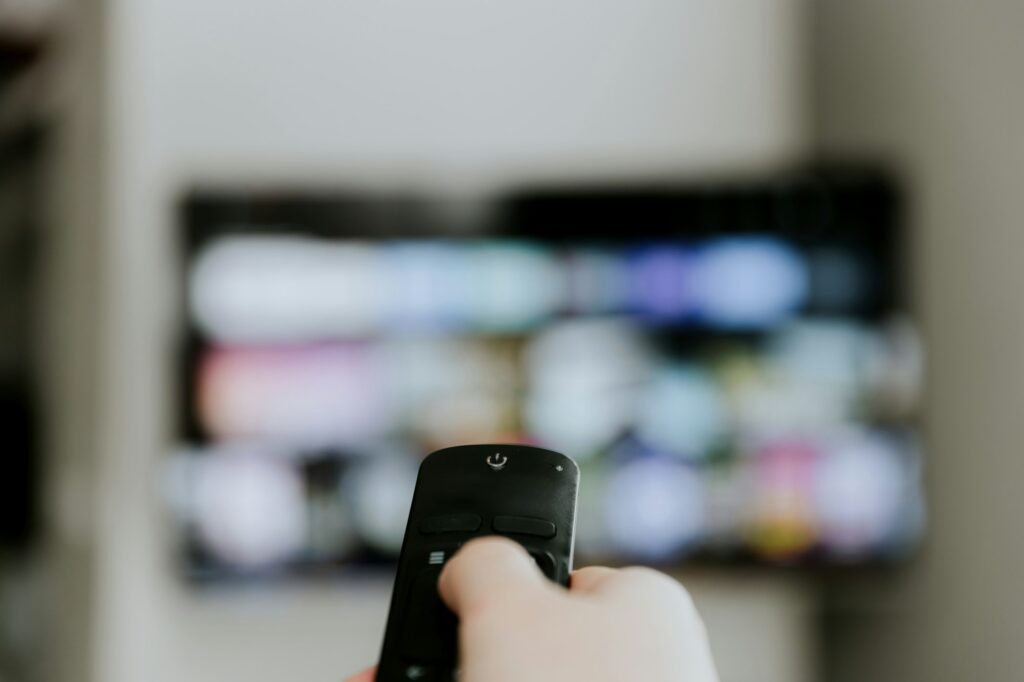 Hand holding remote control pointing to TV. Person watching smart television