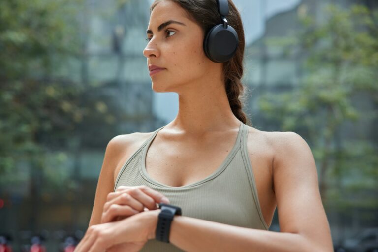 Horizontal shot of thoughtful healthy young woman uses wearable technology sport watch checks burned