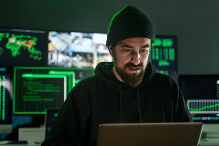 Male hacker with beard working near computer monitors with data on screens on black