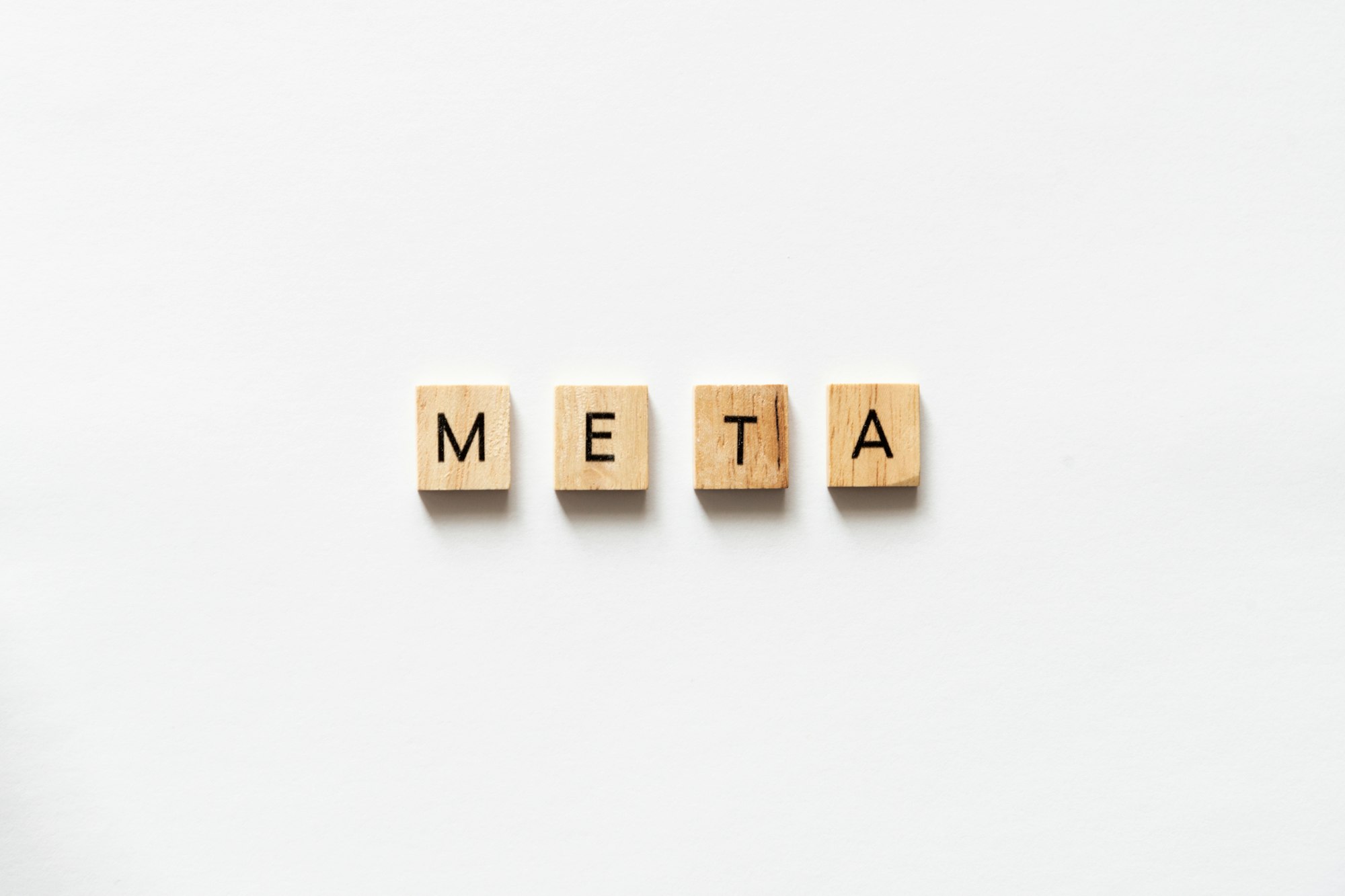 META spelled out with wooden letter tiles on white surface.