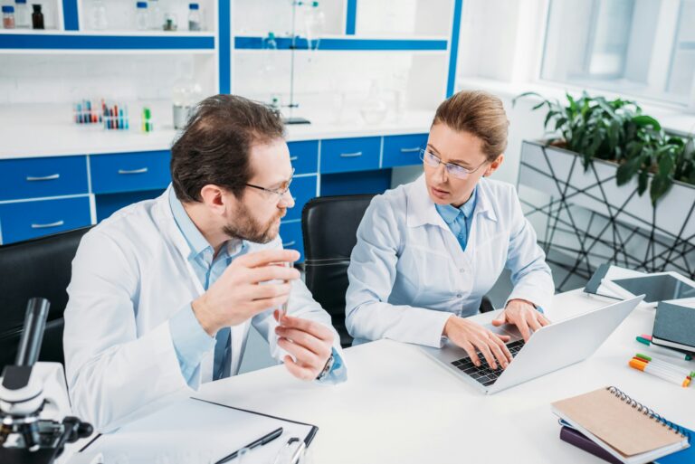 scientific researchers in white coats discussing work at workplace in laboratory