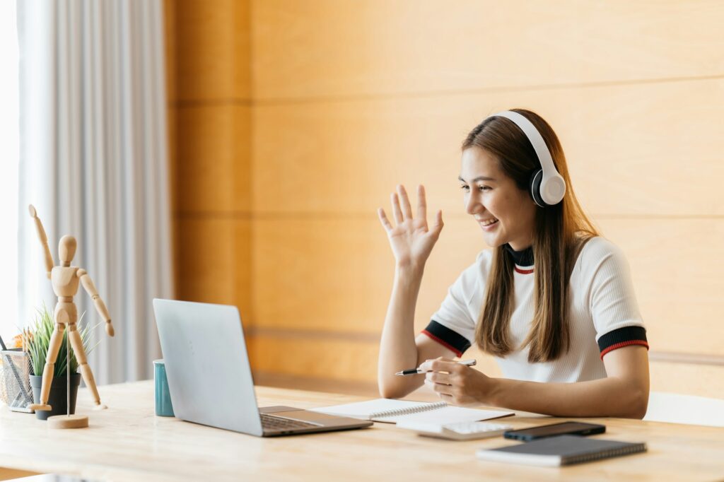 Smiling Asian young female using headset looking at laptop screen listen and learning online courses