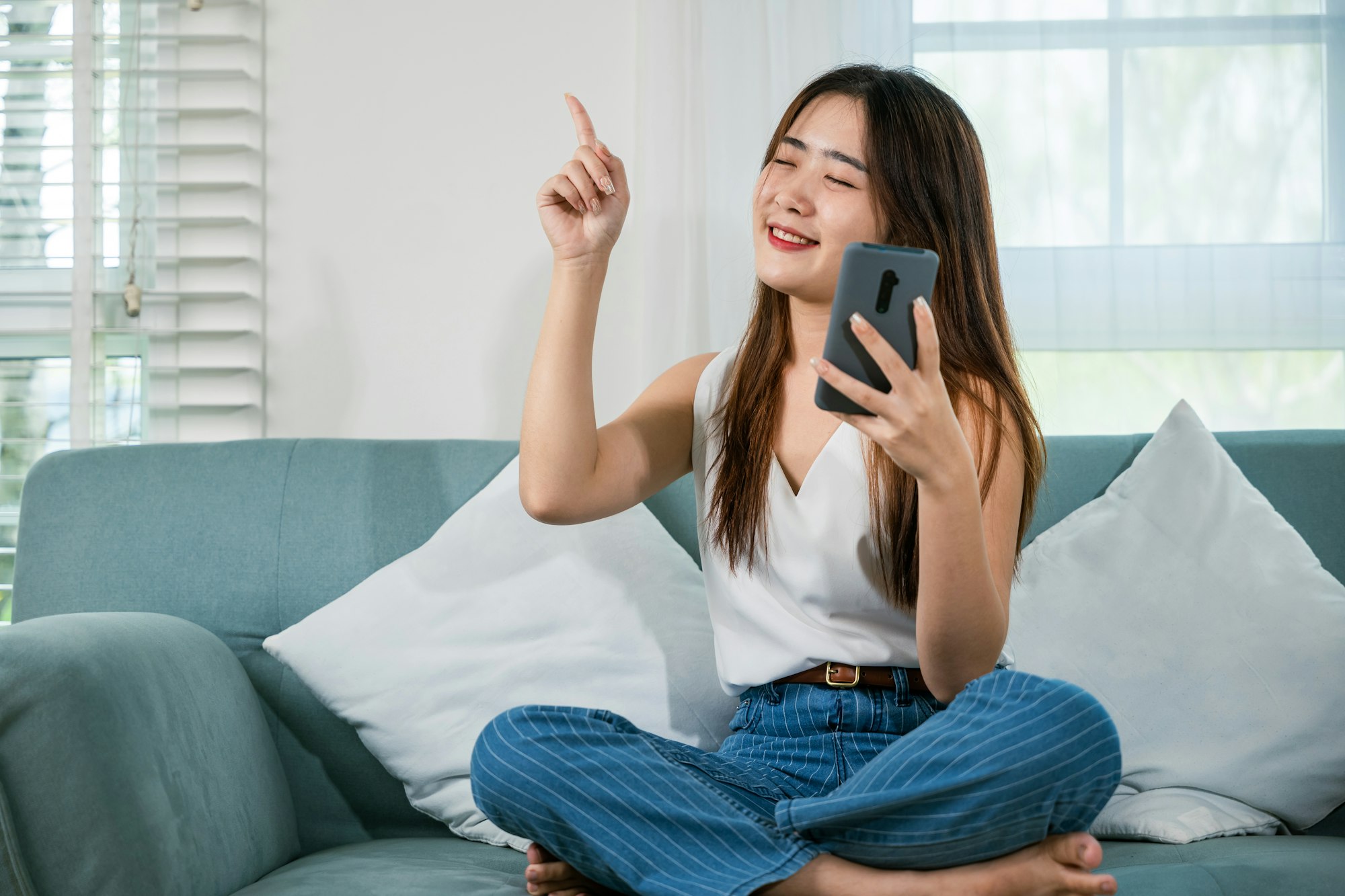 woman wear earbuds listening to music on sofa with smart mobile phone