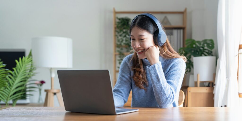 Young asian woman talk on video call at the table using headphones. Online remote work or learning