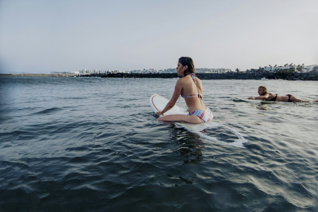 Young girls learning to surf ocean waves at sunset in canary Islands