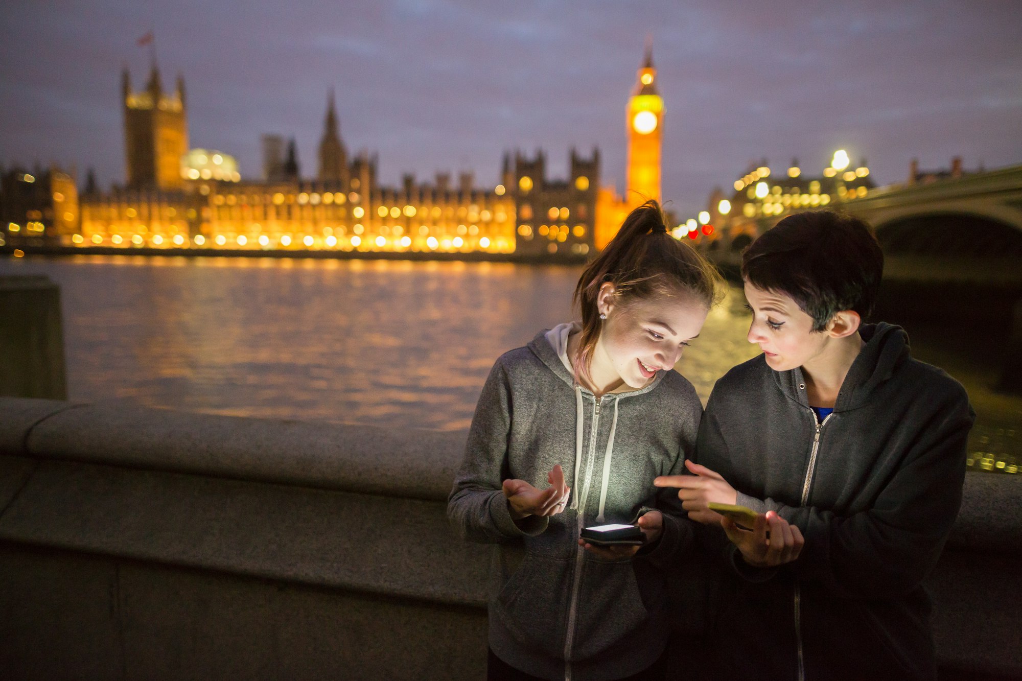 Young women illuminated by smartphone opposite Palace of Westminster, London, UK