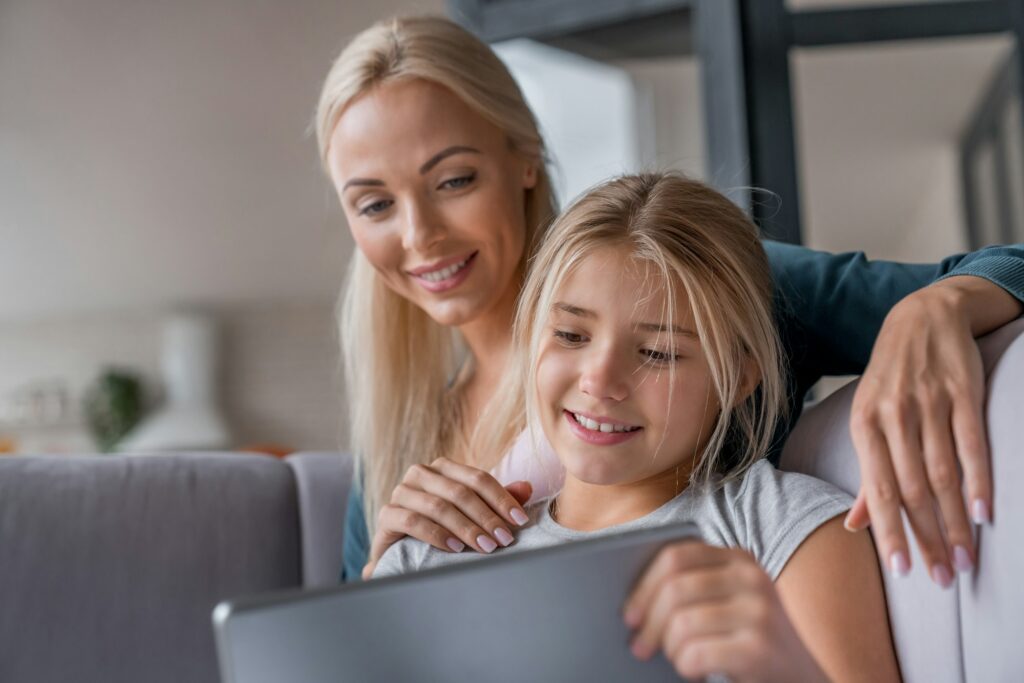 Close up of mother and daughter sitting on sofa and using digital tablet