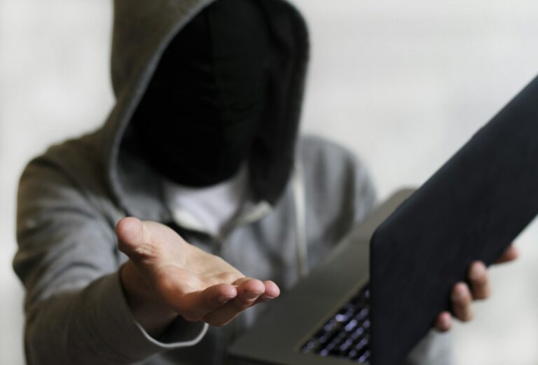 Closeup of an anonymous person with a hood on holding a laptop - cybersecurity concept