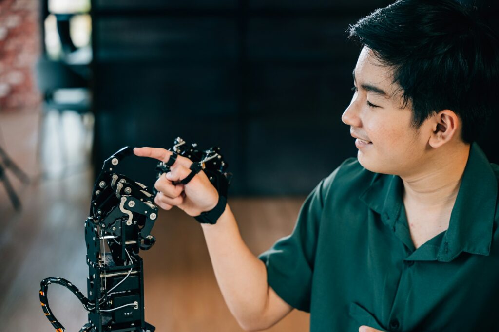 Enthusiastic Asian teen boy learns technology by testing a robot hand and arm in a technical college