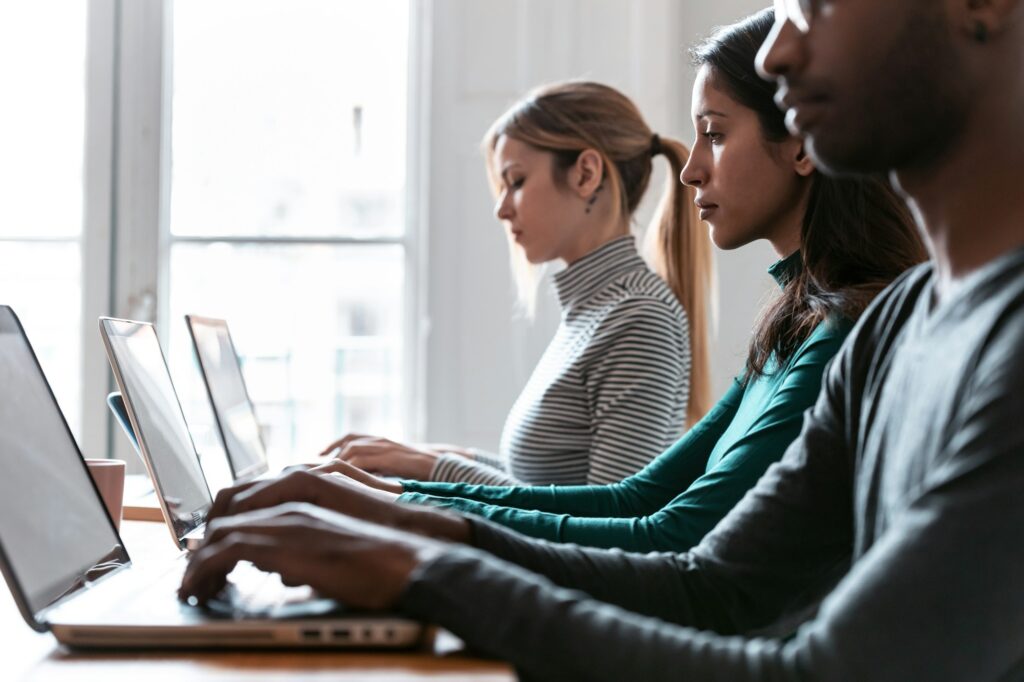 Line of concentrated employees working with laptops on coworking place.