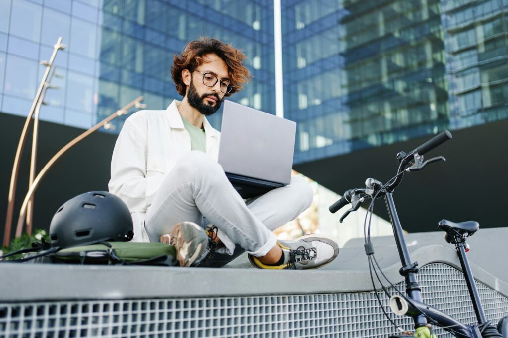 Man working on laptop outside the office, next to bicycle - Young professional tech entrepreneur