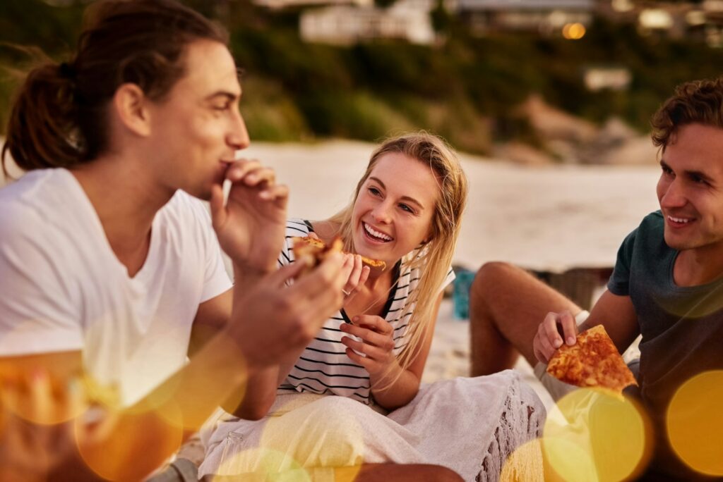 Pizza is happy food. Shot of a group of friends sitting together on the beach.