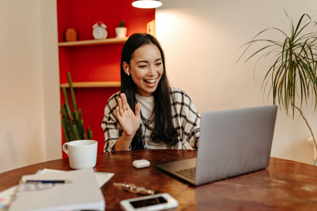 Positive girl in wireless headphones speaks by video link in laptop