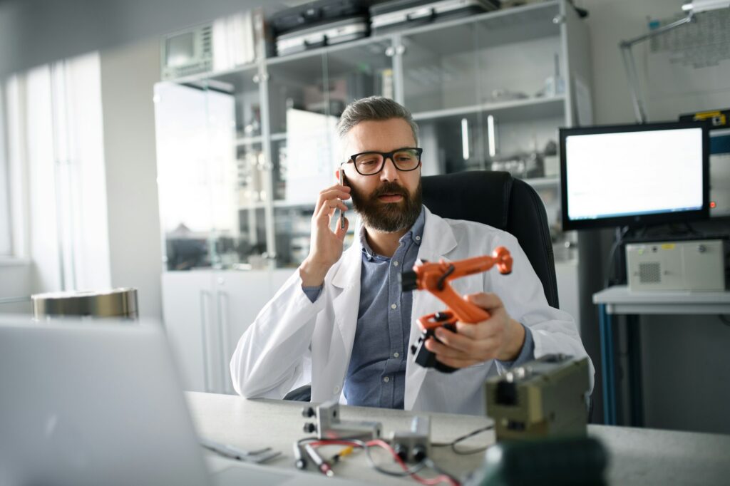 Robotics engineer calling on cellphone and working on desing of modern robotic arm in laboratory