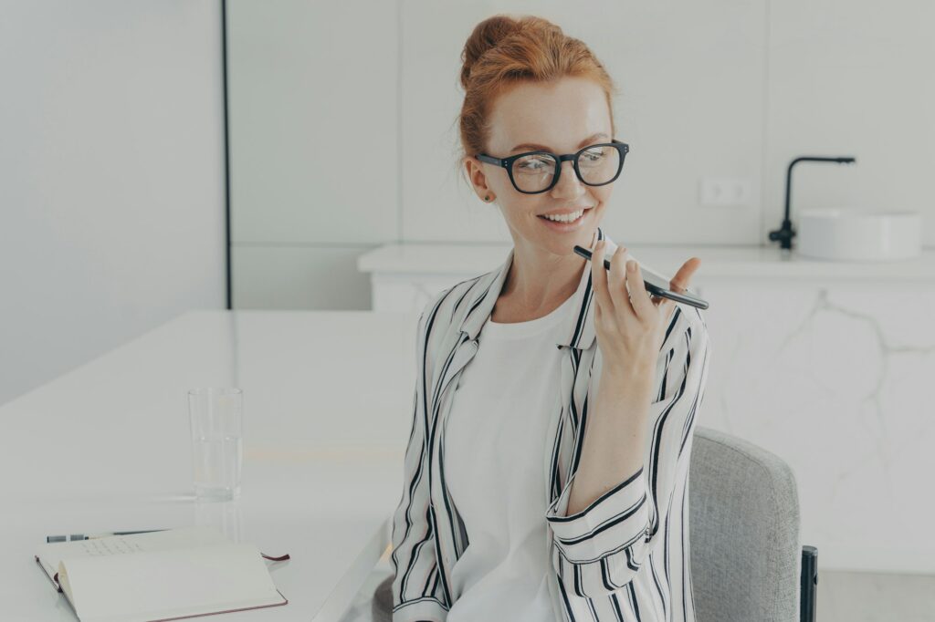 Smiling redhead woman uses virtual voice assistant records audio message