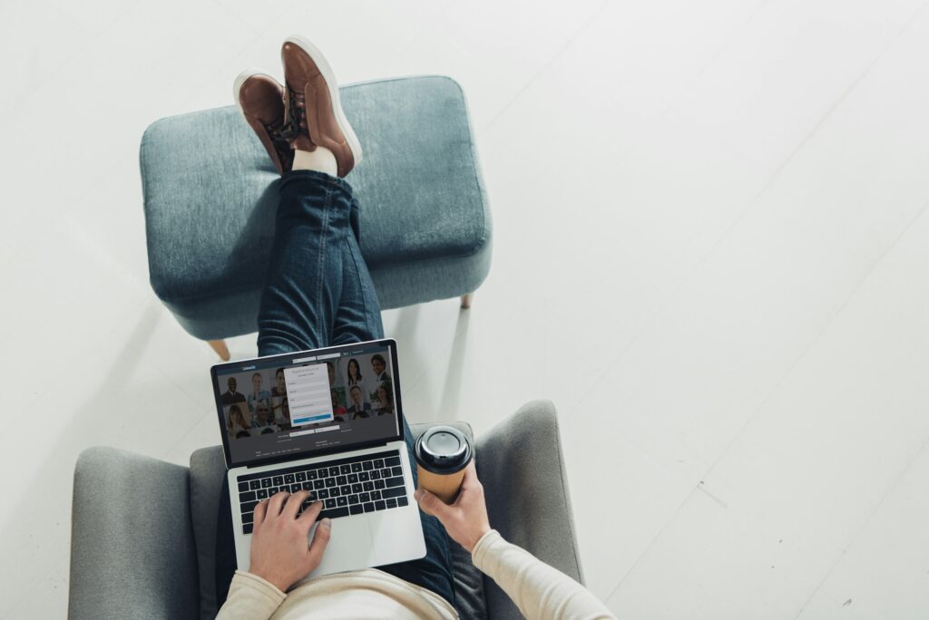 top view of man holding paper cup and using laptop with linkedin website on screen