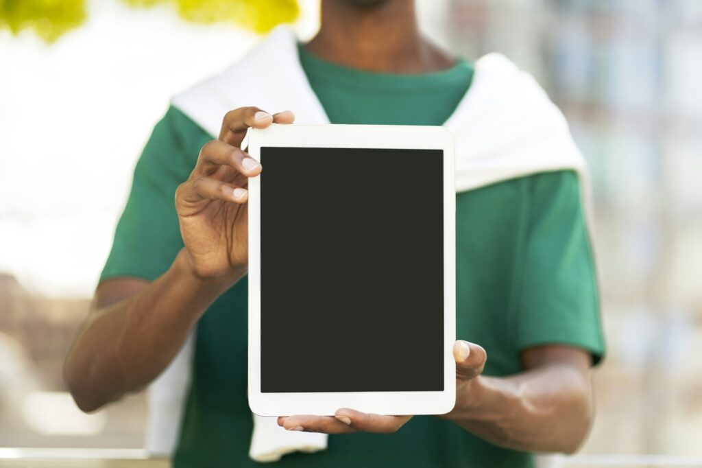 Young man holding digital tablet with blank screen, place for advertising, mockup outdoors