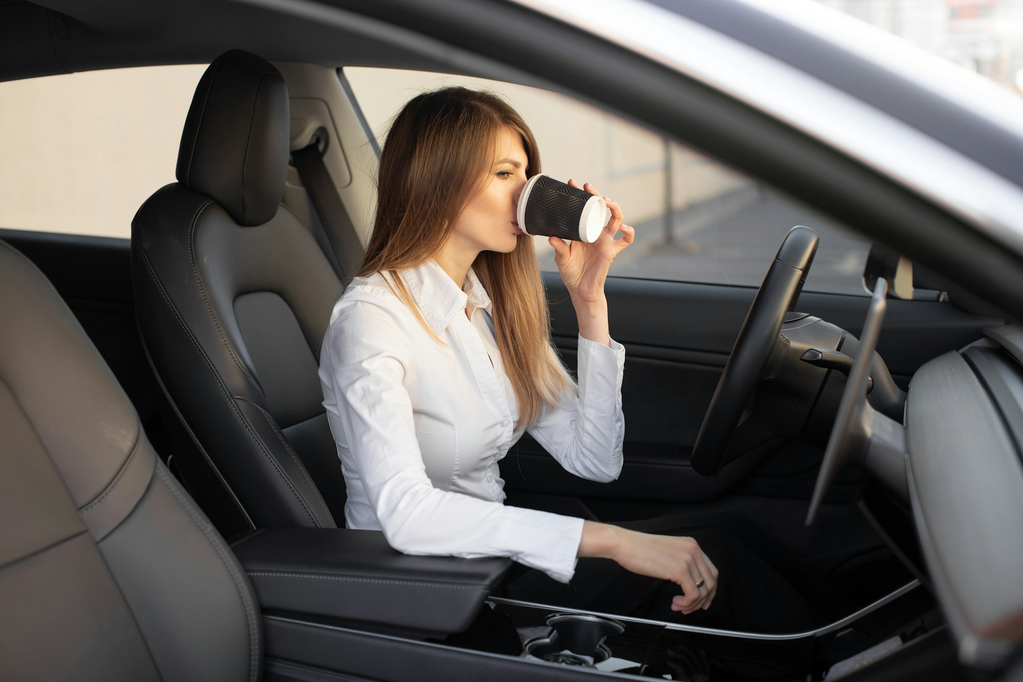 young pretty businesswoman drinking take away coffee, sitting inside of autonomous driverless