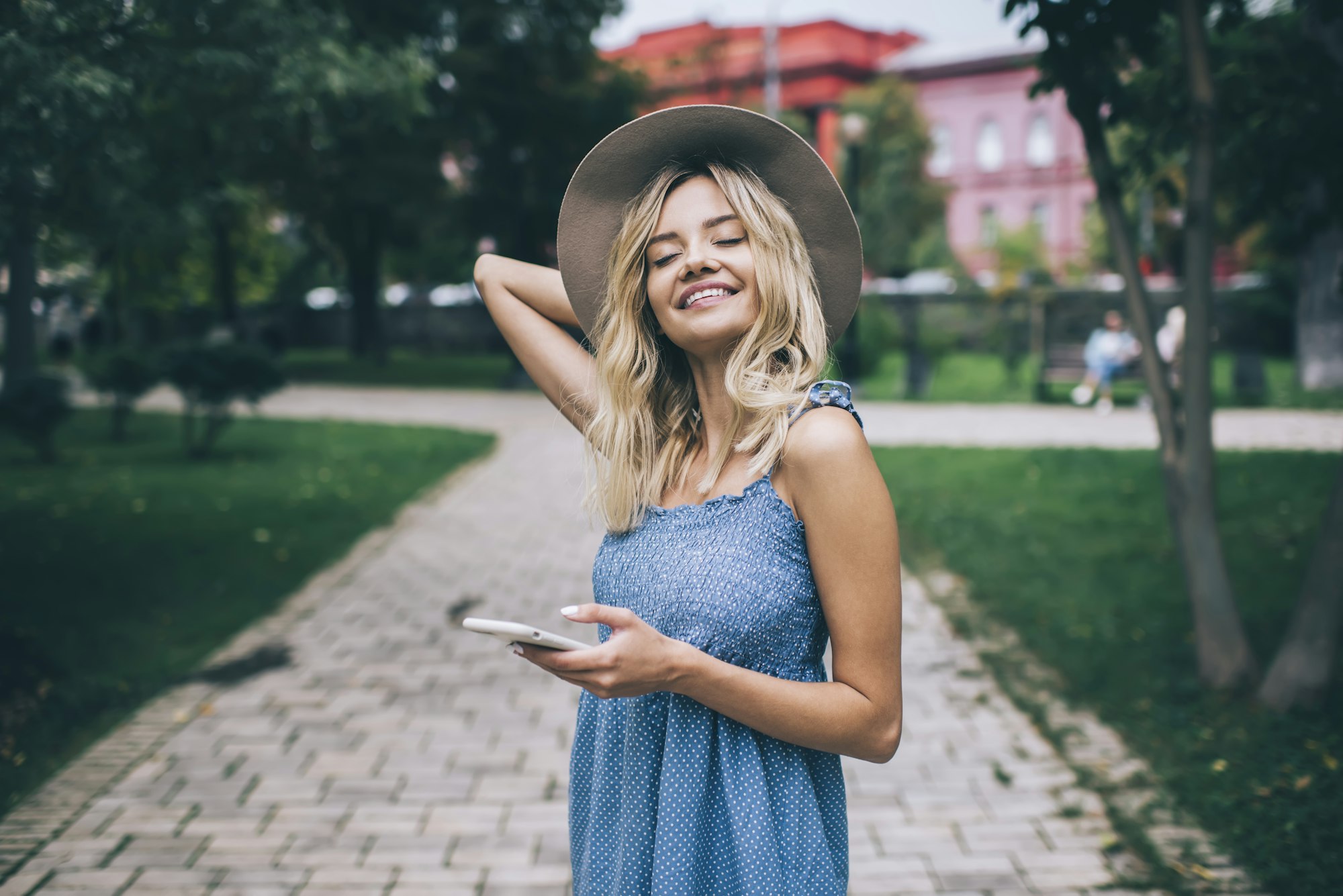 Cheerful Caucasian millennial woman with digital smartphone technology smiling outdoors