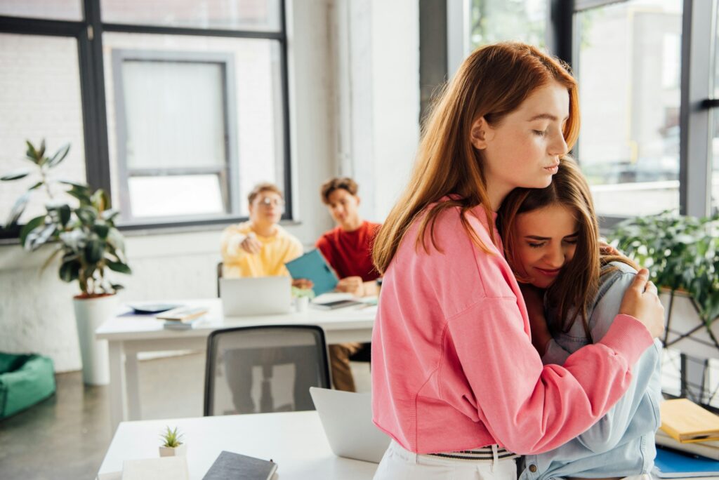 girl supporting and embracing sad friend in school