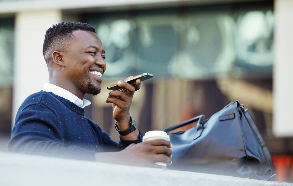 Happy black man talking on phone, travel for business in a city, sitting outside while using tech t