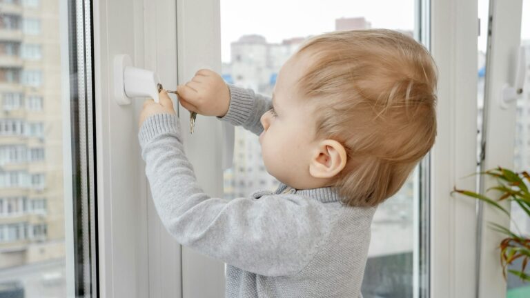 Little baby boy opens window safety lock with key. Baby in danger. Child safety and protection