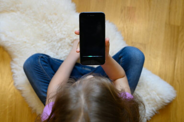 little six year old girl using a smartphone voice recognition online sitting on floor at home