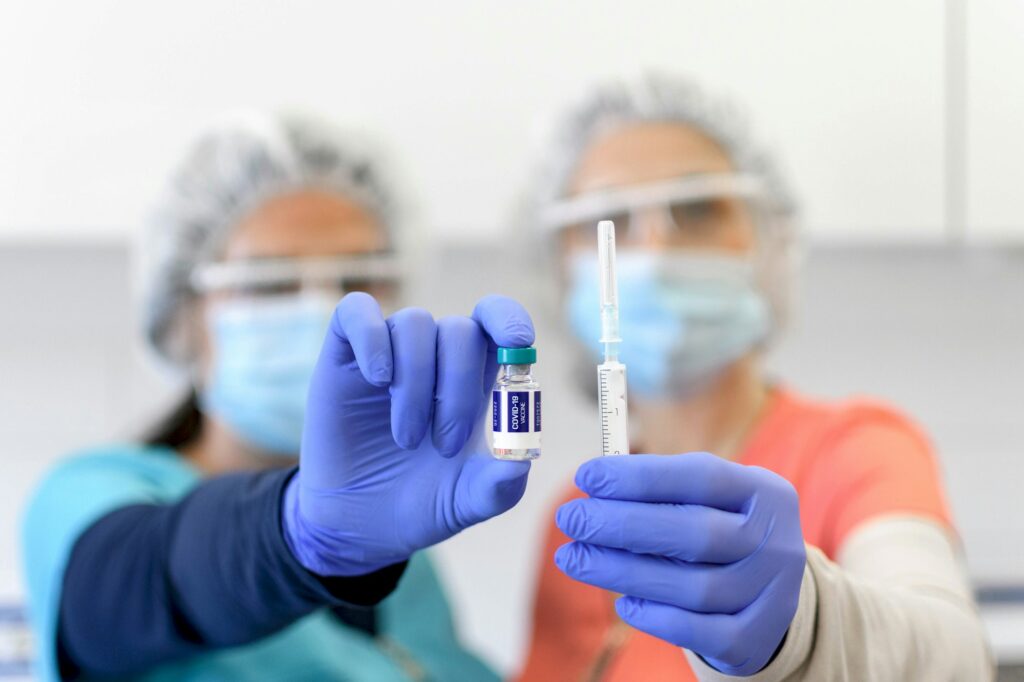 Selective focus image of Two nurses wearing protective masks, holding vaccine and syringe, covid.