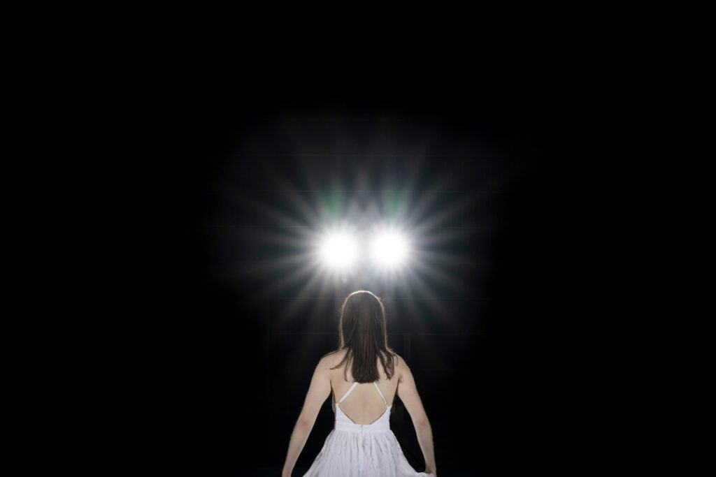 View of a woman in a white dress from behind looking into two bright spotlight flash lights with a b