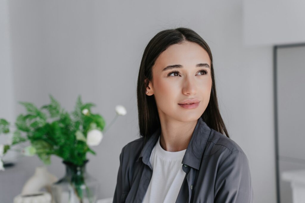 young purposeful woman in grey shirt looking aside over blurry interior with flowers.