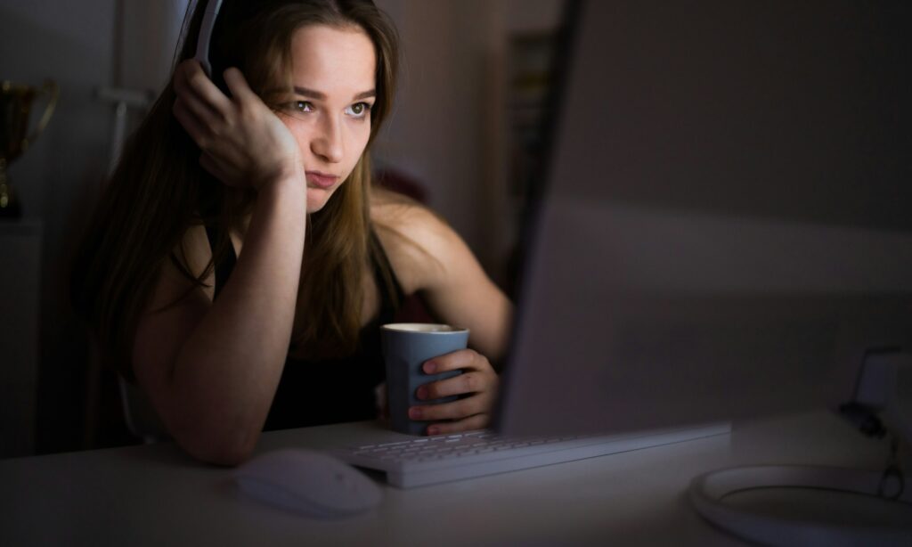 Bored young girl with computer sitting indoors, internet abuse concept