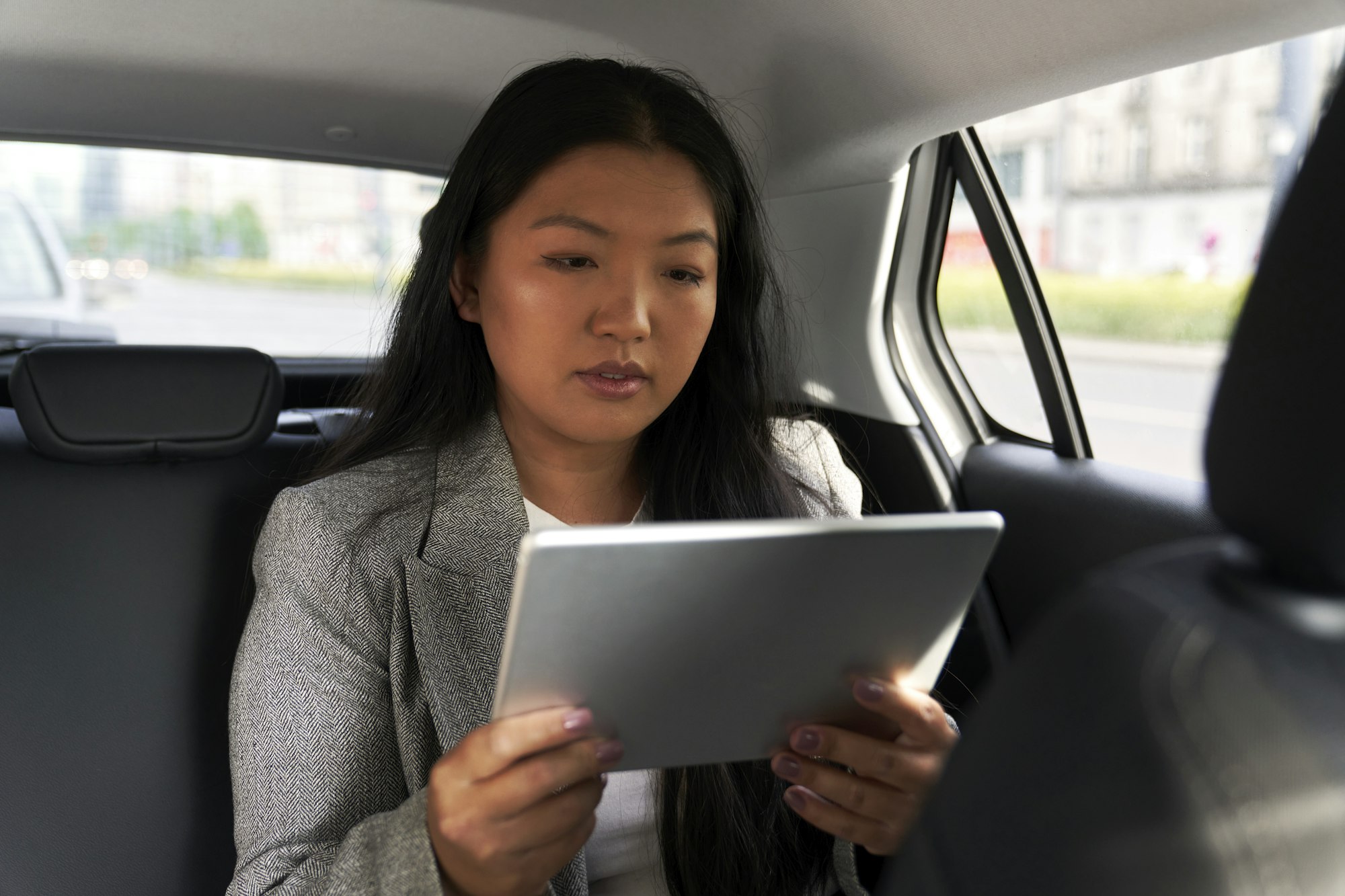 Business Chinese woman driving in a taxi and browsing digital tablet