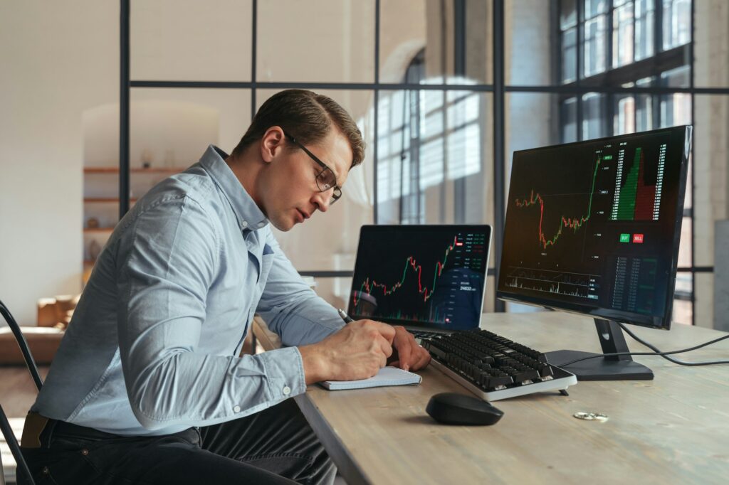 Crypto trader noting down info in notepad after checking ico and trading market dynamics on PC