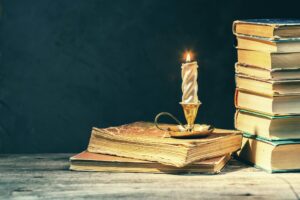 Dark Academia study at night background with old books stacked and vintage candle holder.