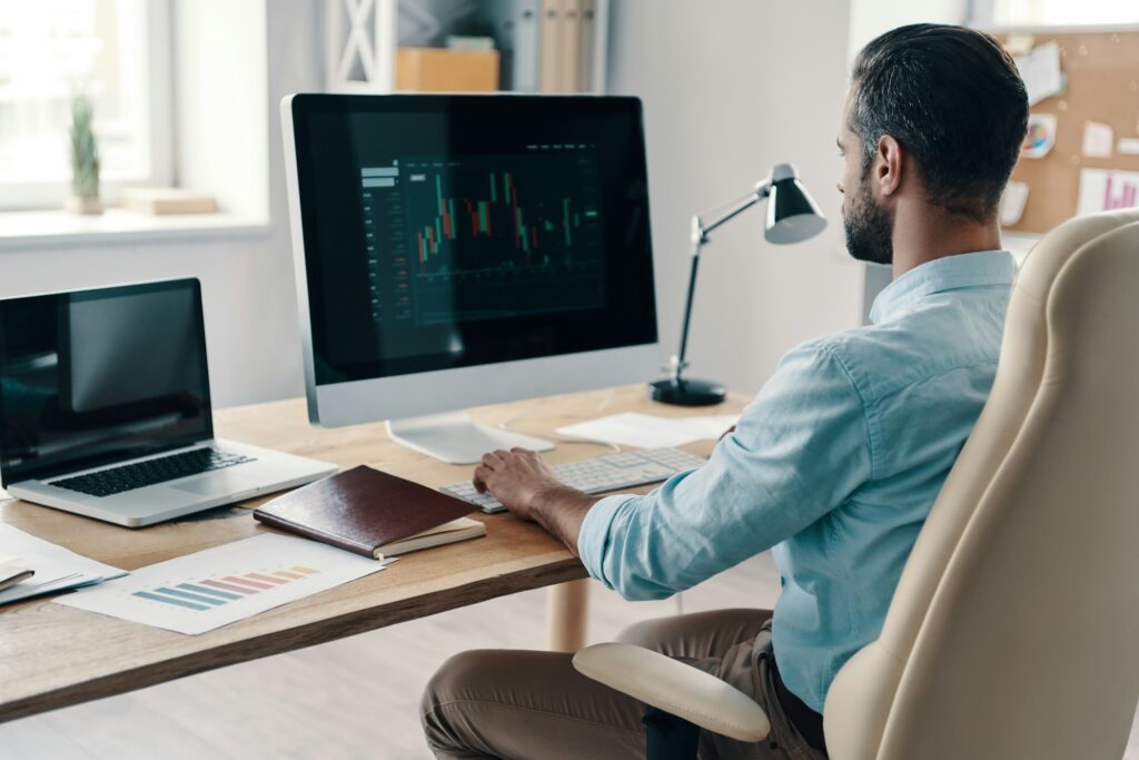 Efficiency. Young modern businessman analyzing data using computer while sitting in the office