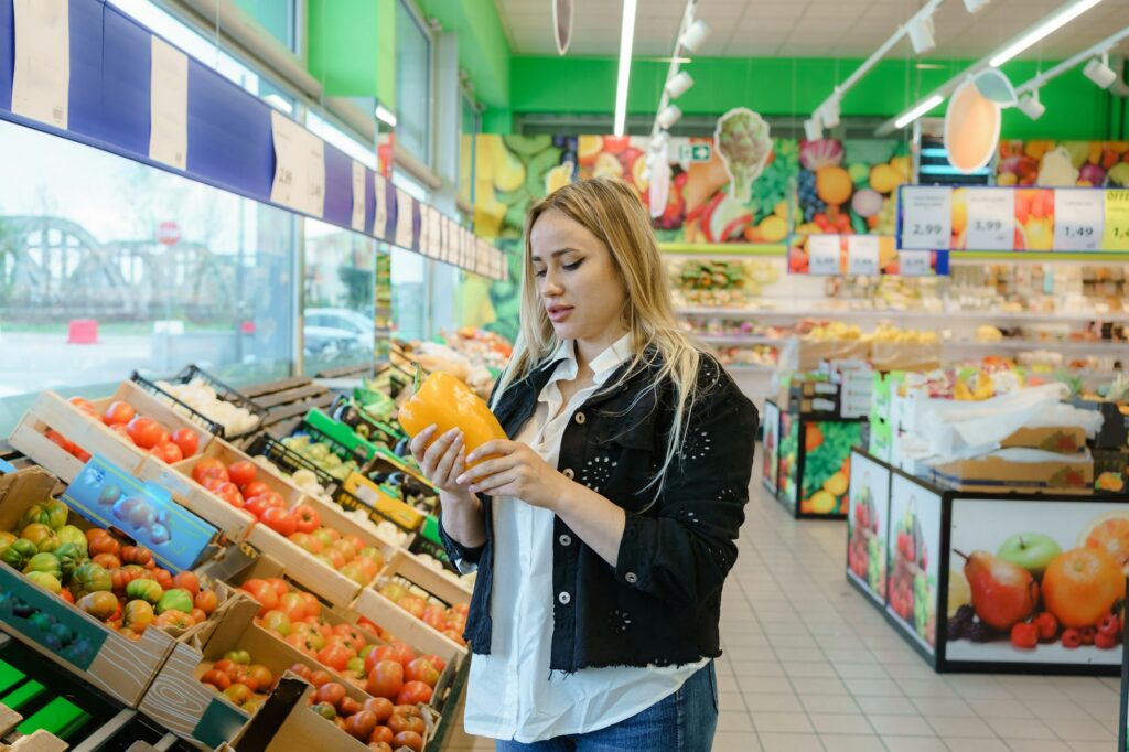 Experience the joy of a woman in the supermarket, smiling while holding a fresh, healthy pepper.