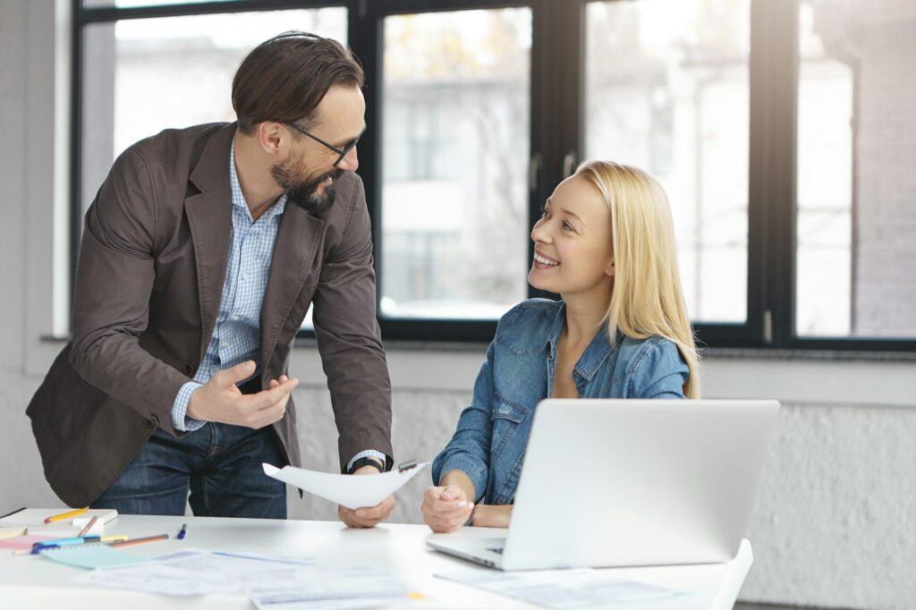 Handsome mature male financier and his female secretary work with documents, discuss something activ