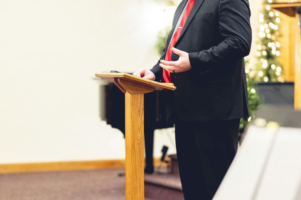 Male wearing a black suit and preaching holding onto a pulpit