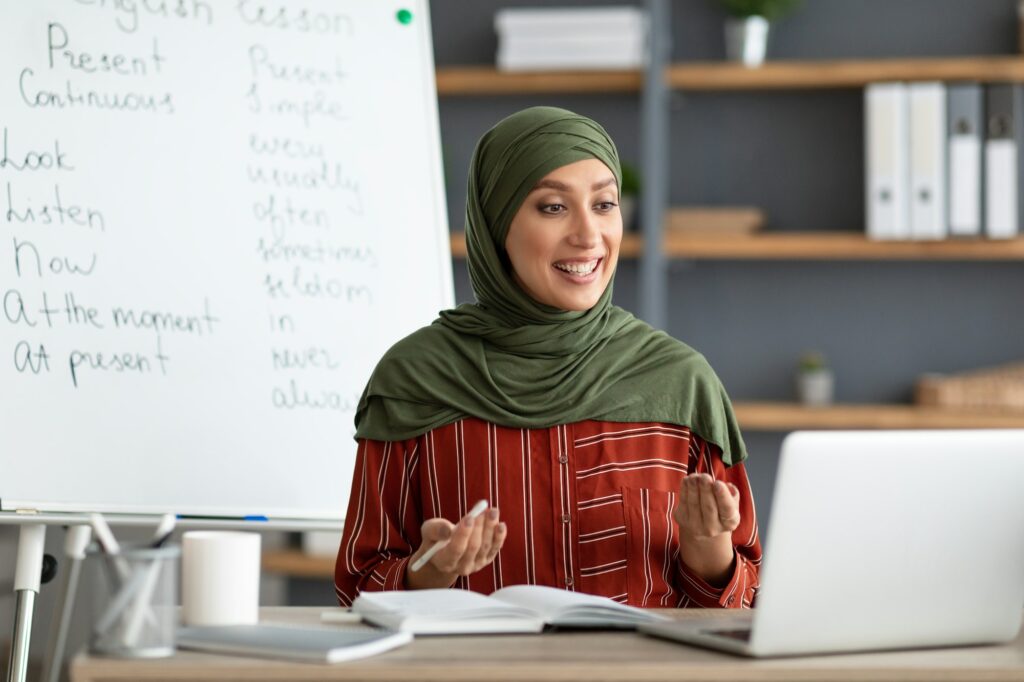 Muslim English teacher making videocall, explaining lesson to students