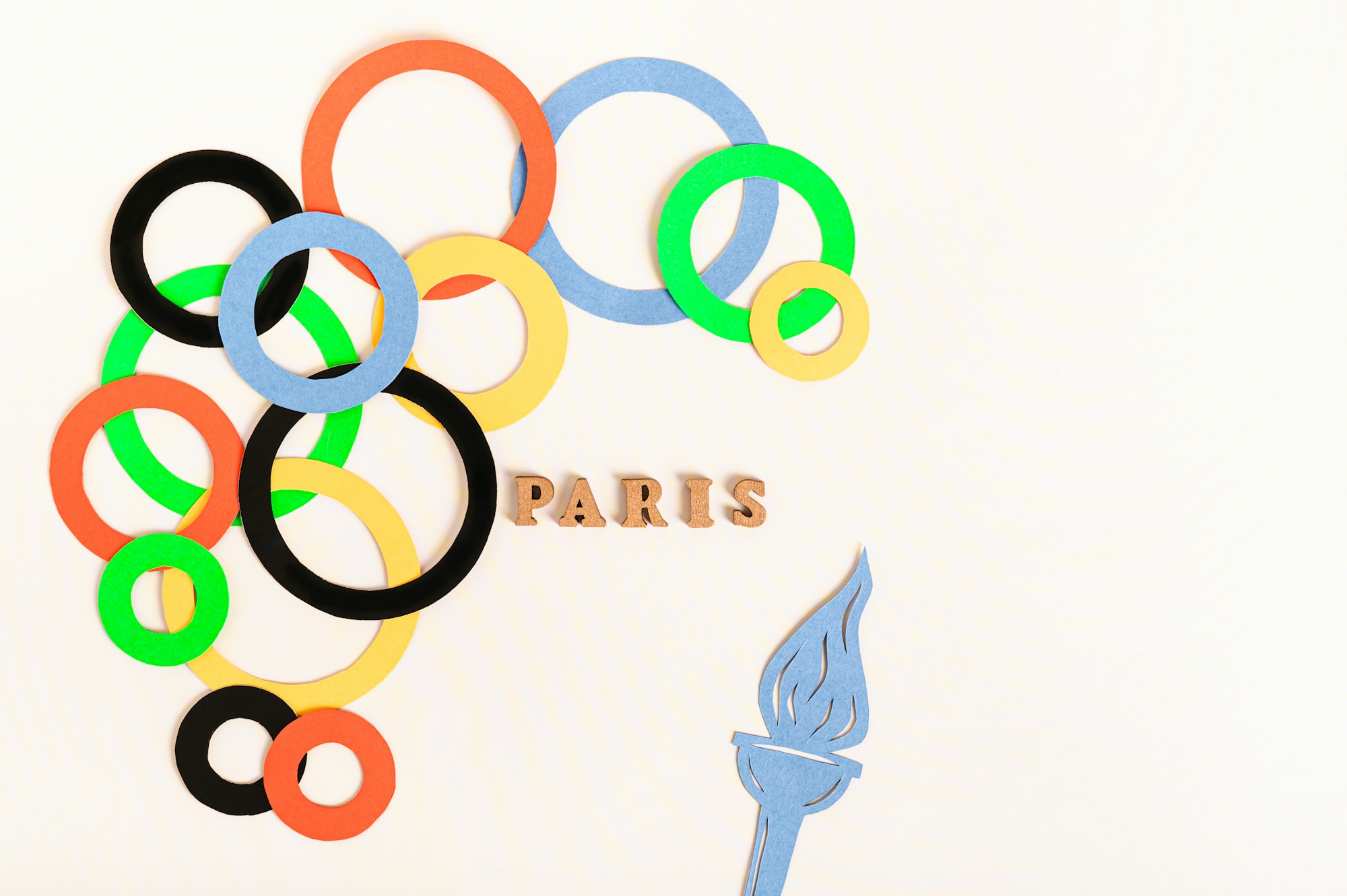 olympics, paris, france, summer, multi colored rings around the text and a flame on a light