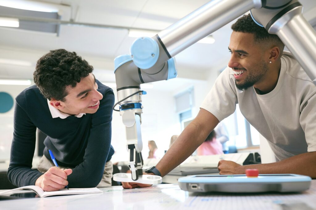 Two Male College Or University Engineering Students In Robotics Class Working On Robot Arm