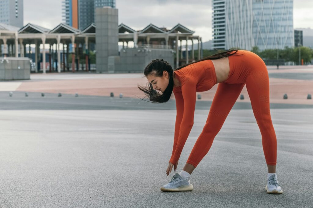 Young female athlete stretching hamstrings before jogging. Caucasian woman warm up before workout.