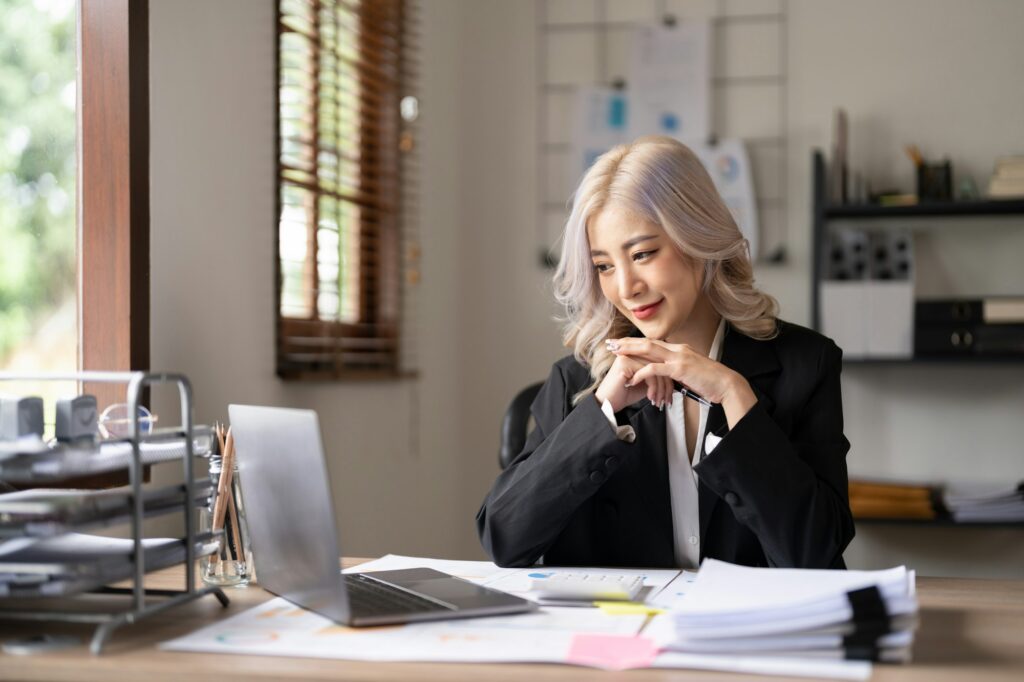 Young finance market analyst working at sunny office on laptop while sitting at wooden table