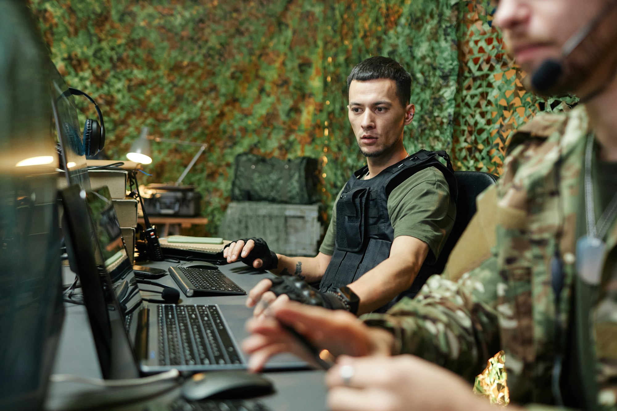 Young serious male military officer in body armor sitting by workplace