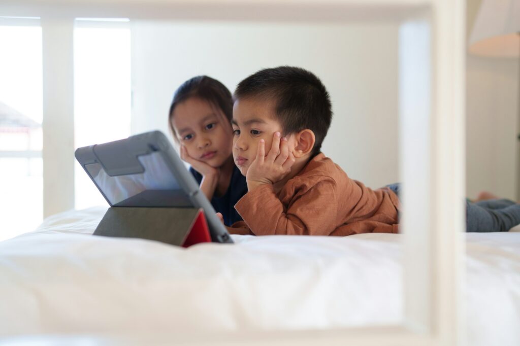 Asian little sibling watching video clip on tablet together in the bedroom.