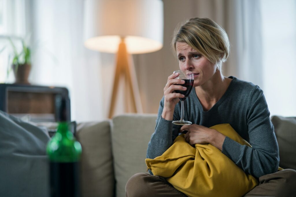 Depressed woman with wine indoors at home, mental health and alcohol addiction concept.