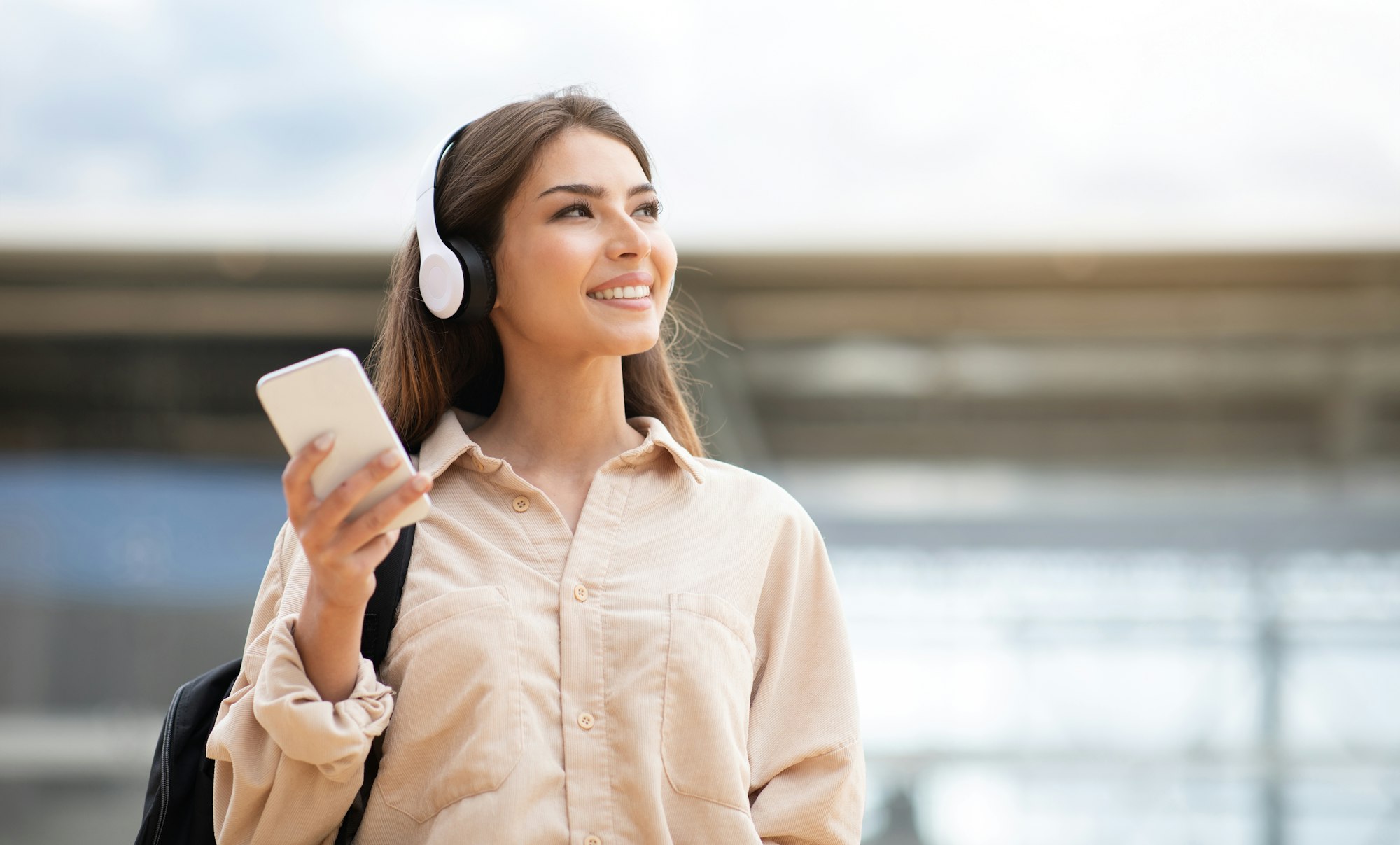 Lady with wireless headphones and mobile phone listening music outside